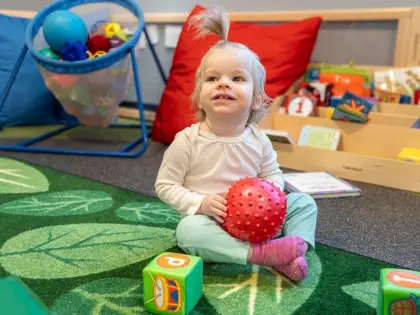 Little girl sitting on the floor holding a red ball
